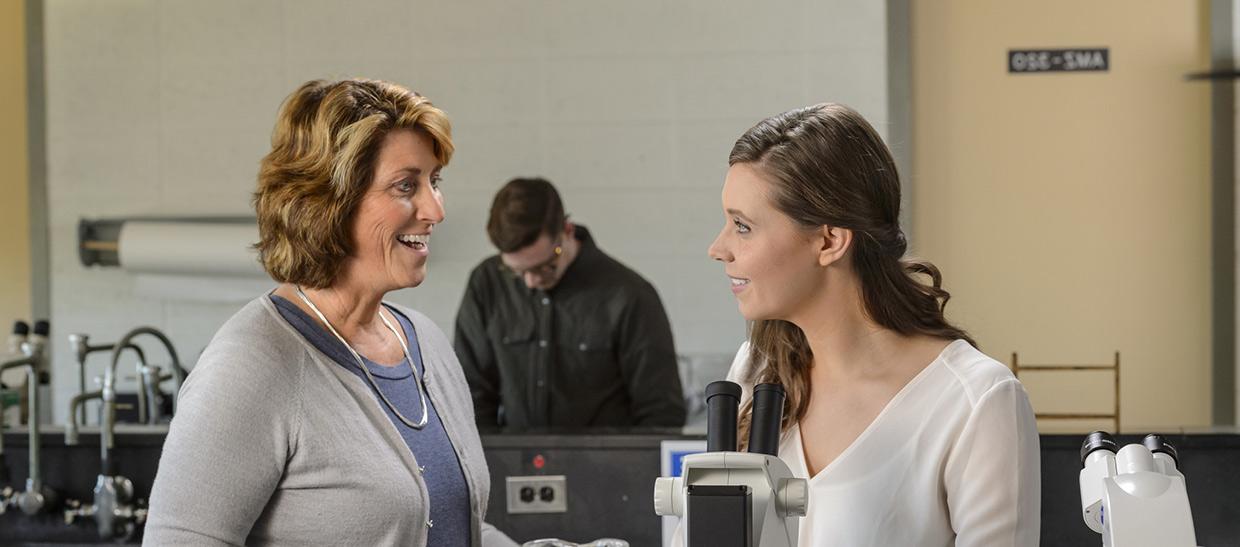 Student looking in microscope in lab with professor